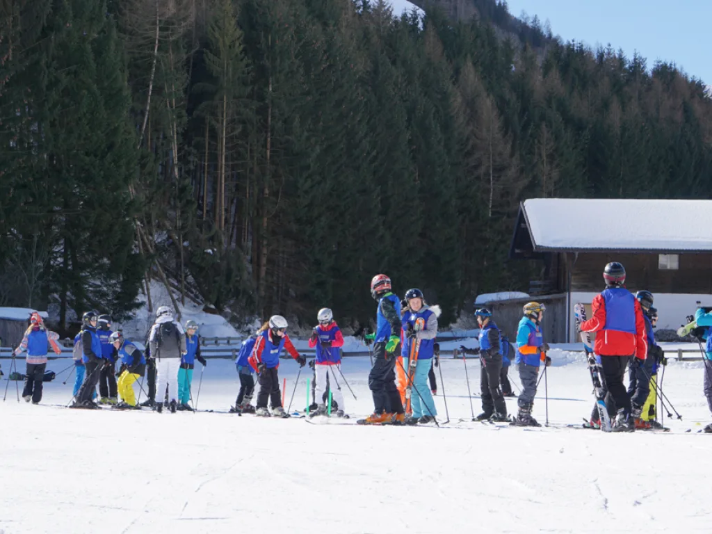Skigruppe sammelt sich am Hangfuß vor einem Gebäude.